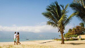A beach with a palm tree, a clear sky, and a distant view of mountains. - Hotel do Sol Executive (São Sebastião)