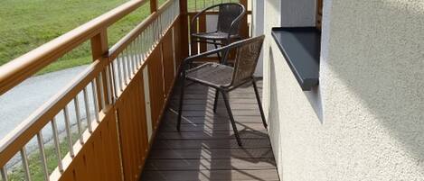 A wooden deck with a metal railing, a chair, and a small table.