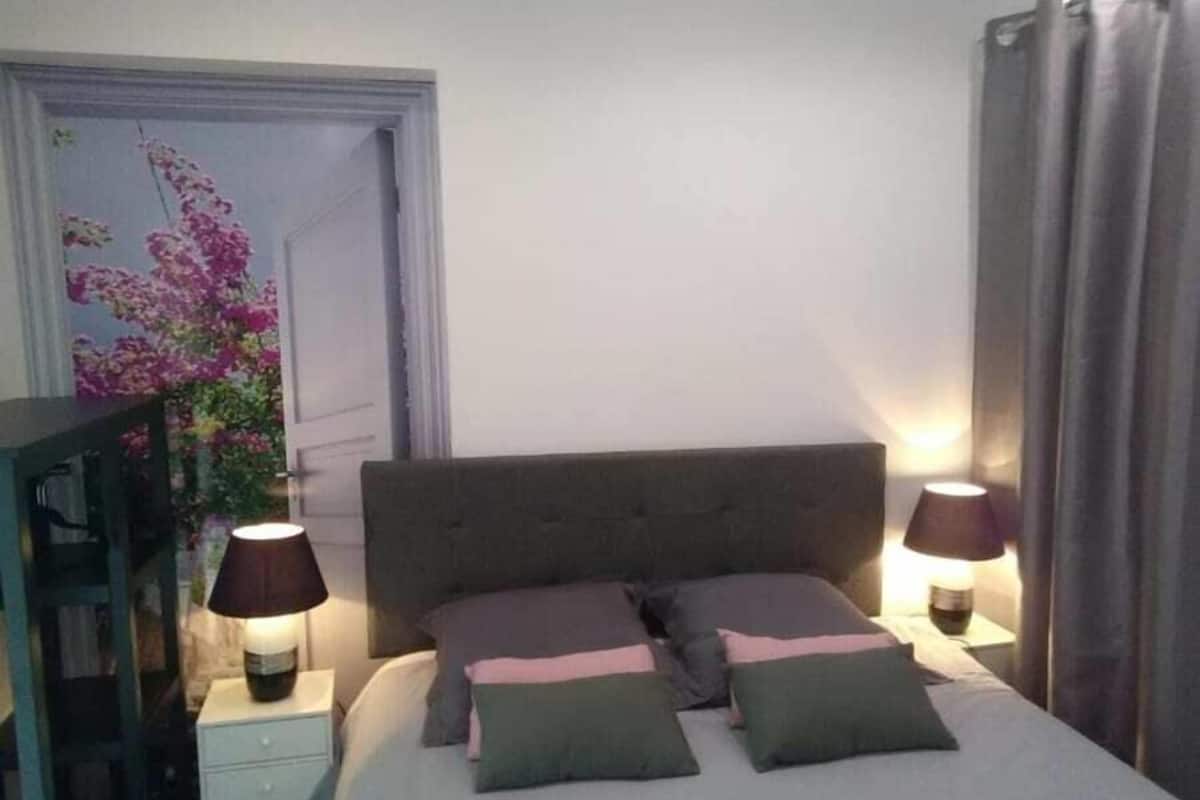 A neatly made bed with a grey headboard, two bedside lamps, and a floral wall decoration.