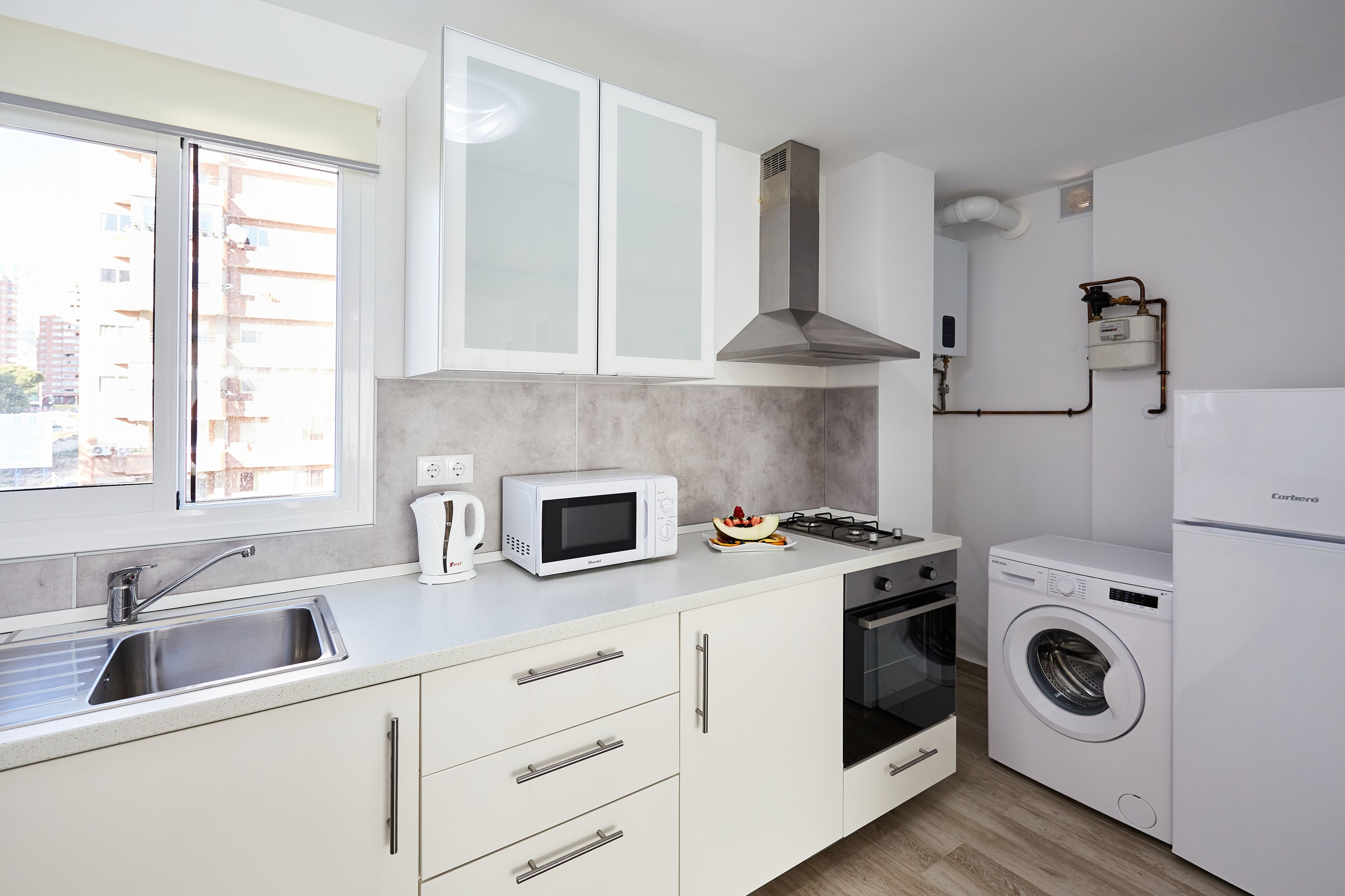 Una cocina moderna con armarios blancos, microondas, estufa, fregadero y lavadora.
