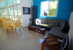 Una sala de estar con un sofá, una mesa de centro y un juego de mesa. Se ve un ventanal con vistas al exterior.