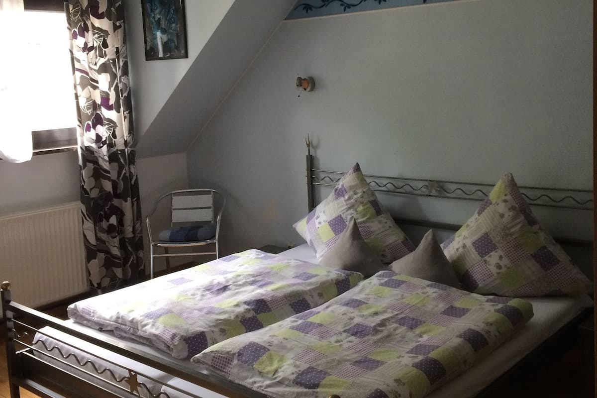 A bedroom with a bed, a chair, a radiator, and a window with curtains.