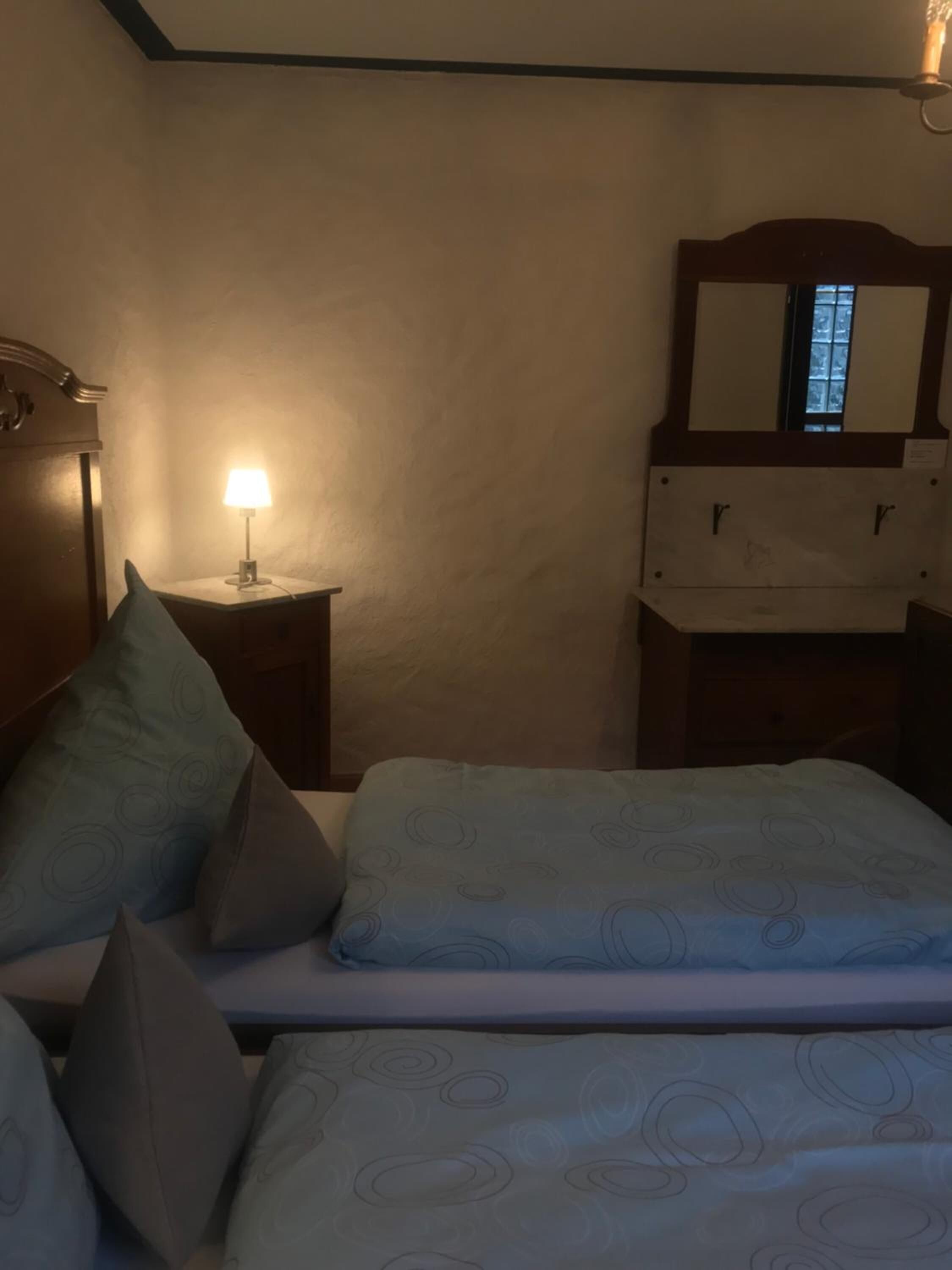 Ein Schlafzimmer mit einem Bett, Kissen, einem Nachttisch mit Lampe, einem Schminktisch und einem Spiegel.