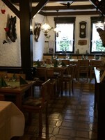A restaurant interior with wooden tables and chairs, stone flooring, and hanging light fixtures.