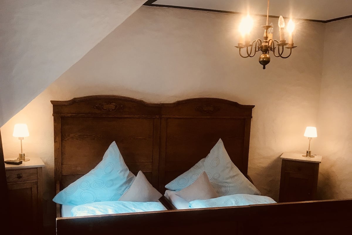 A bedroom with a wooden headboard, two bedside tables with lamps, and a chandelier.
