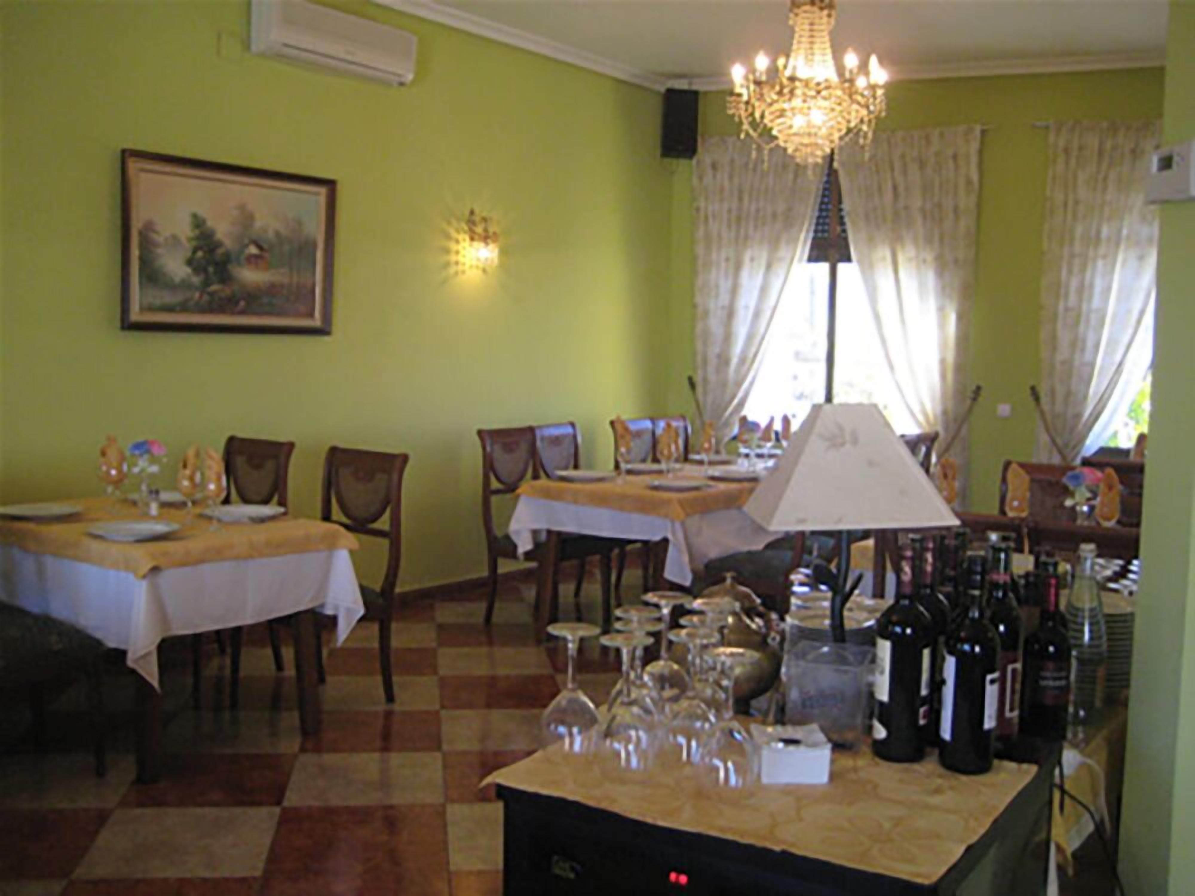 Un comedor con mesas dispuestas para comidas, una araña y una vinoteca con botellas.