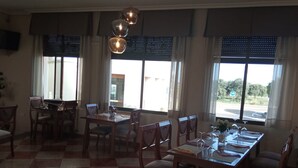 Un área de comedor con piso a cuadros, mobiliario de madera y ventanas amplias con persianas.