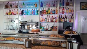Una zona de bar con estantes llenos de botellas de licores, una máquina de café y una presentación de pasteles y pan.