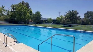 Una piscina azul cristalina con barandales metálicos y un borde con baldosas.