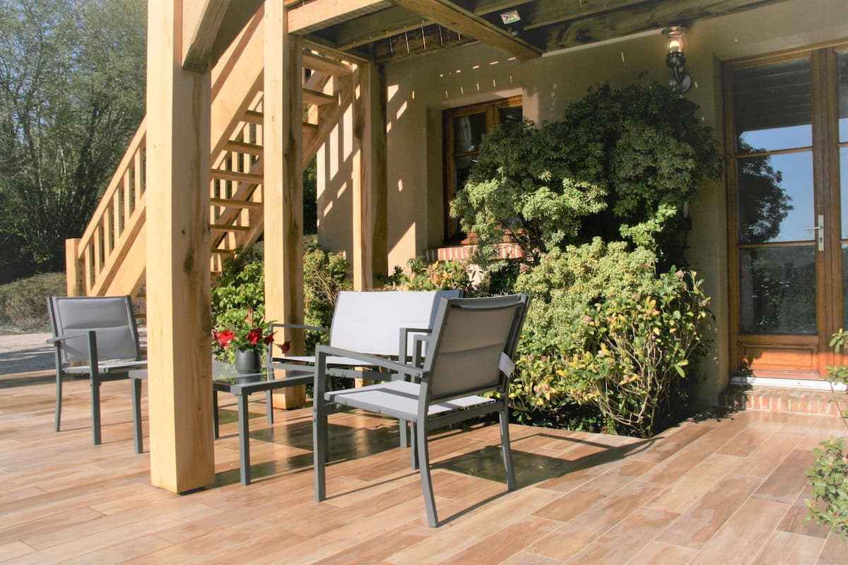 An outdoor patio with two chairs and a table, surrounded by a wooden pergola and lush greenery.