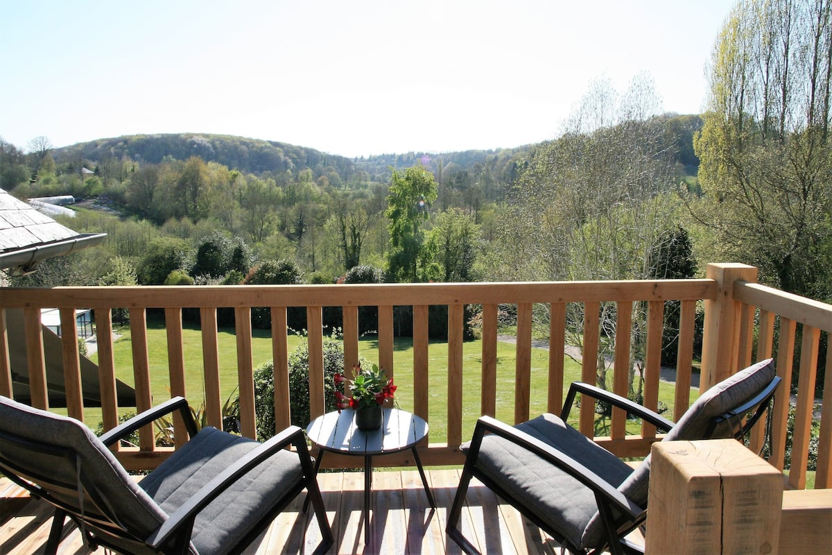 A wooden deck with two chairs and a table, overlooking a green landscape with hills.