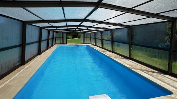 Una piscina larga y rectangular en el interior, con paredes de vidrio transparente y suelo de madera.