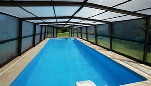 Una piscina larga y rectangular en el interior, con paredes de vidrio transparente y suelo de madera.