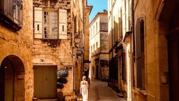 A narrow street with stone buildings, a woman walking, and a sign for 'Hotel Alchelejo'.