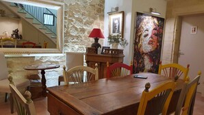 Un comedor con una mesa de madera, sillas, una lámpara roja, un retrato enmarcado y una escalera.