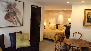 Una habitación de hotel con cama, sofá, mesa de comedor con sillas y obras de arte en las paredes.