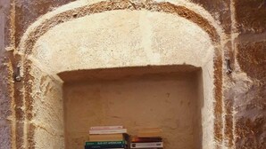 Una estantería de madera con una parte superior en forma de corazón, ubicada en un pequeño rincón con una pared de piedra rugosa.