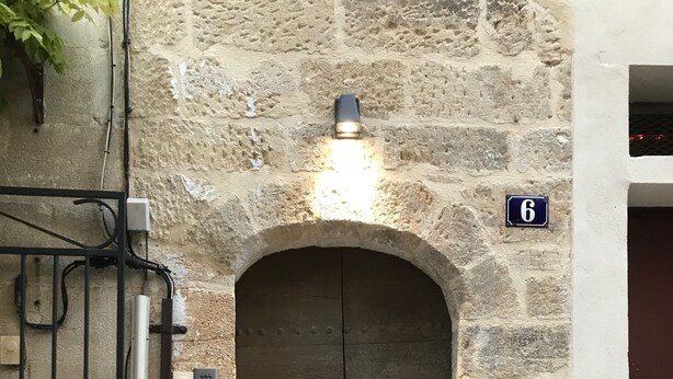 Un edificio de piedra con una puerta de madera, una reja metálica y un cartel con número.