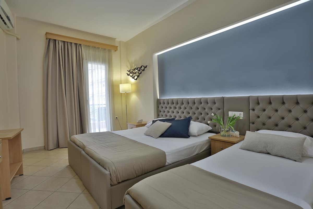 A hotel room with two beds, a large window with curtains, a wall-mounted light, and a decorative wall piece.