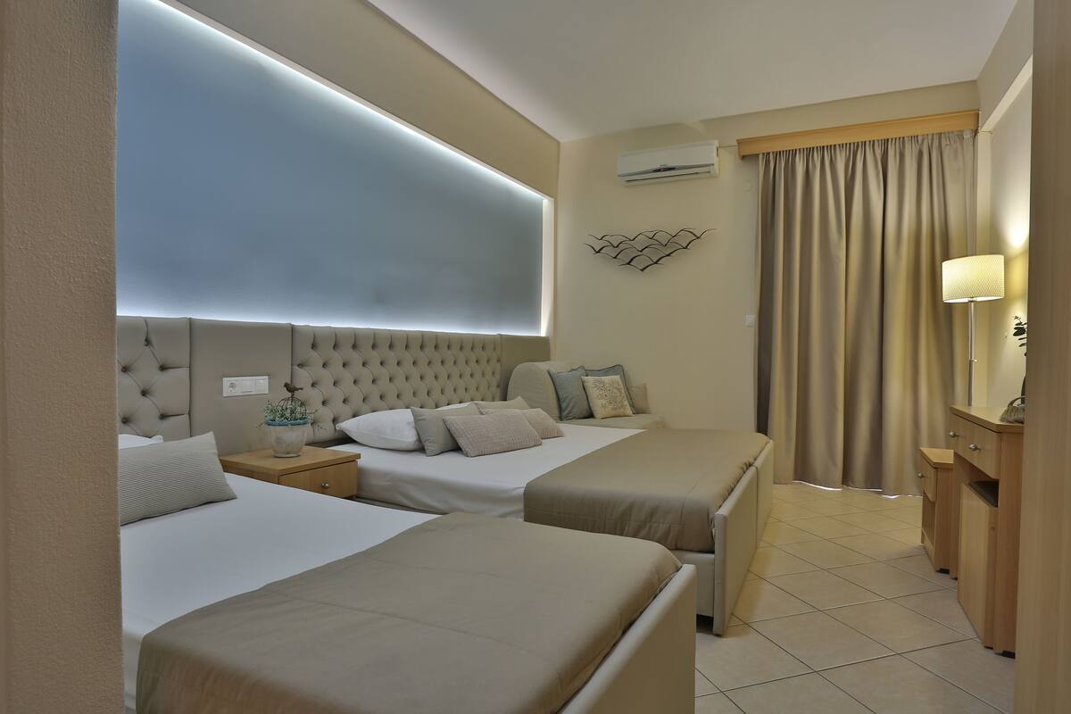 A hotel room with two beds, a bedside table with a lamp, a wall-mounted air conditioner, and a curtain.