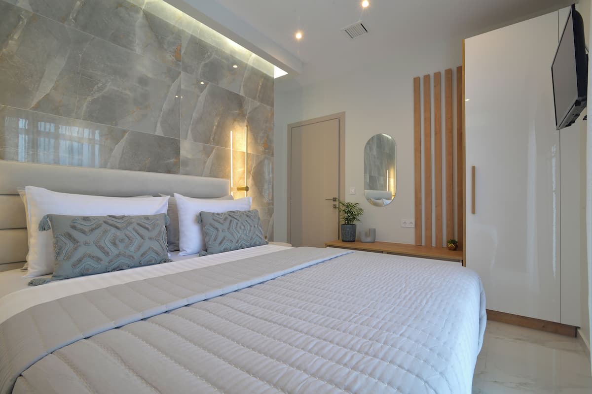 A modern bedroom with a large bed, a marble wall, a wooden nightstand, a mirror, and a wardrobe.