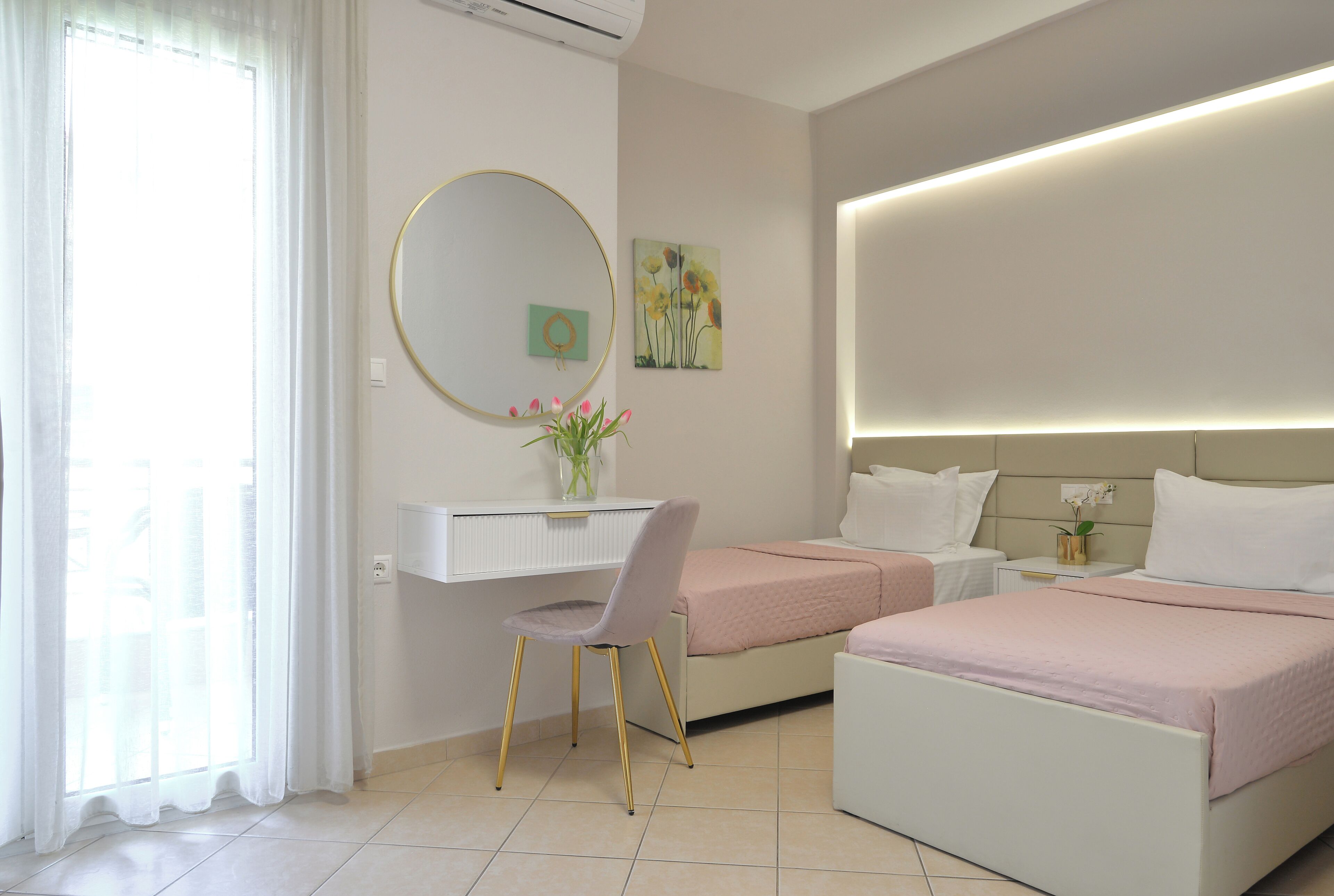 A hotel room with a desk, two beds, a round mirror, and artwork on the walls.
