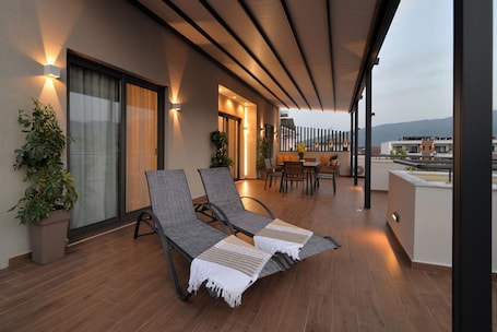 A balcony with two lounge chairs, a table, and chairs, a potted plant, and a view of the cityscape.
