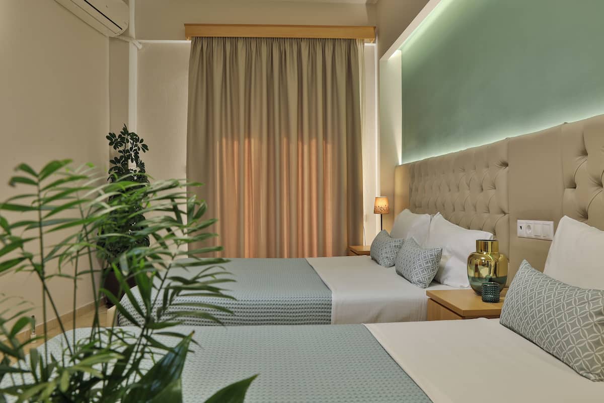 A hotel room with two beds, a large window with curtains, a bedside lamp, and a potted plant.