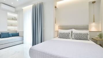 A modern bedroom with a large bed, a sofa, a bedside table with a lamp, and a wall-mounted shelf.
