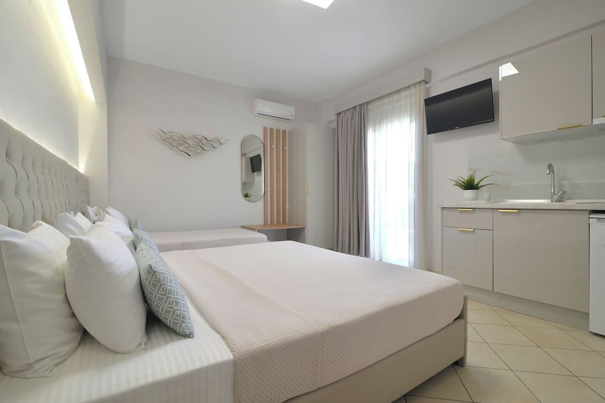 A modern hotel room with a large bed, a small kitchenette, a flat-screen TV, and a window with curtains.