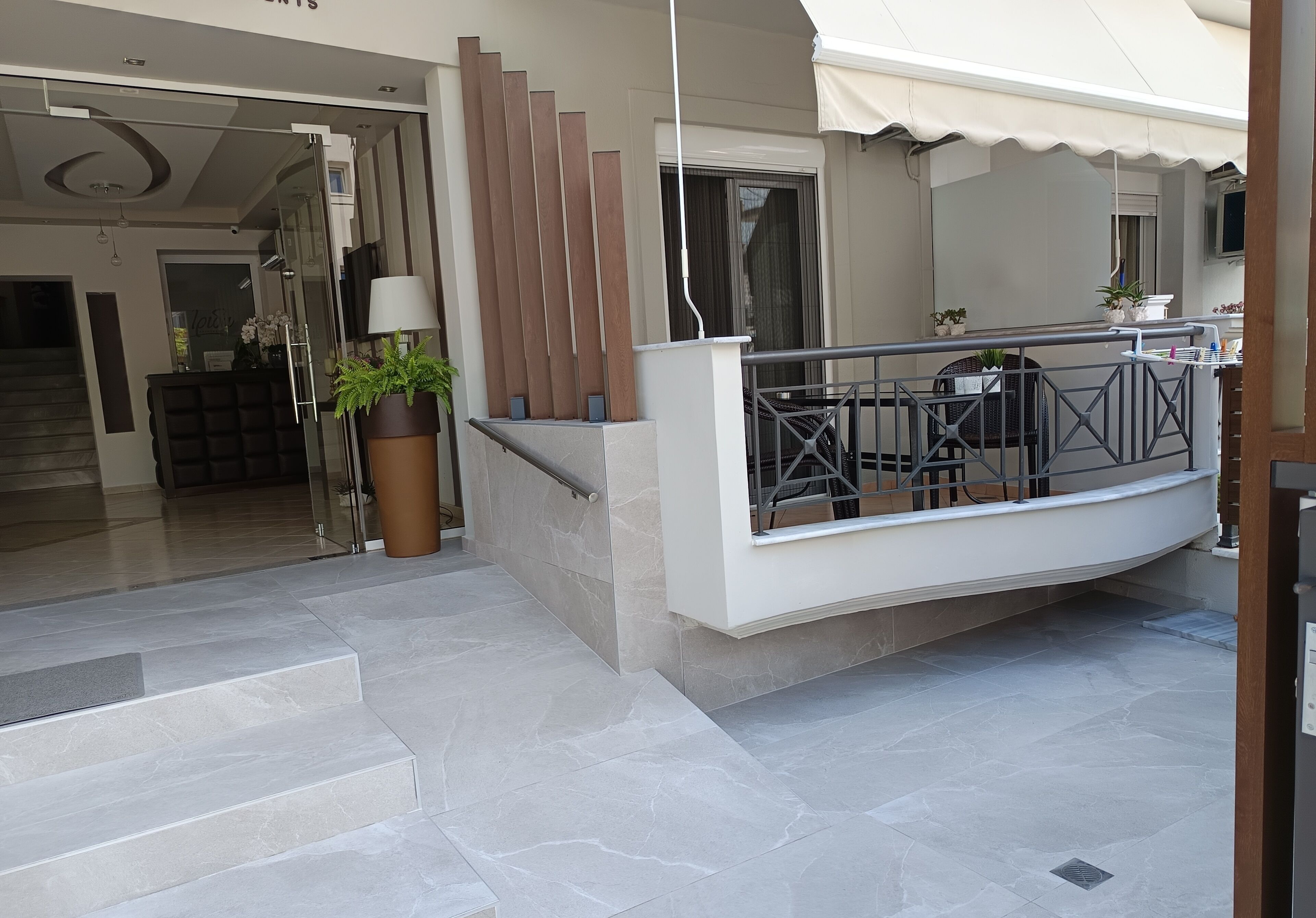 A modern hotel entrance with a glass door, a potted plant, and a staircase leading to the interior.