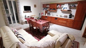 Una sala de estar con sofá, una mesa de comedor y una zona de cocina con armarios de madera y salpicadero de azulejos.