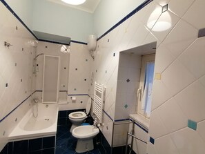 A bathroom with a bathtub, toilet, and bidet, featuring a tiled floor and walls with a geometric pattern. - B&B Eracle (Ercolano)
