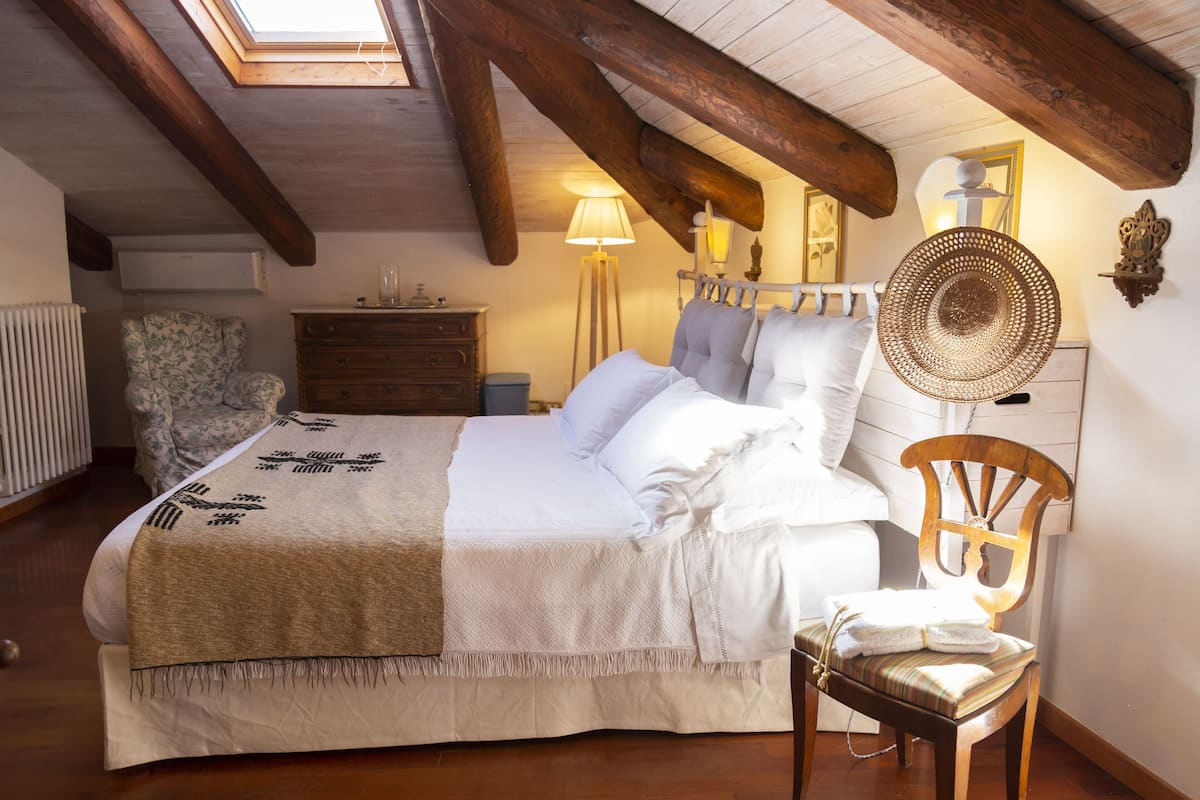 Ein Schlafzimmer mit einem Bett, einem Sessel, einer Kommode, einer Lampe und einem wandmontierten Spiegel.