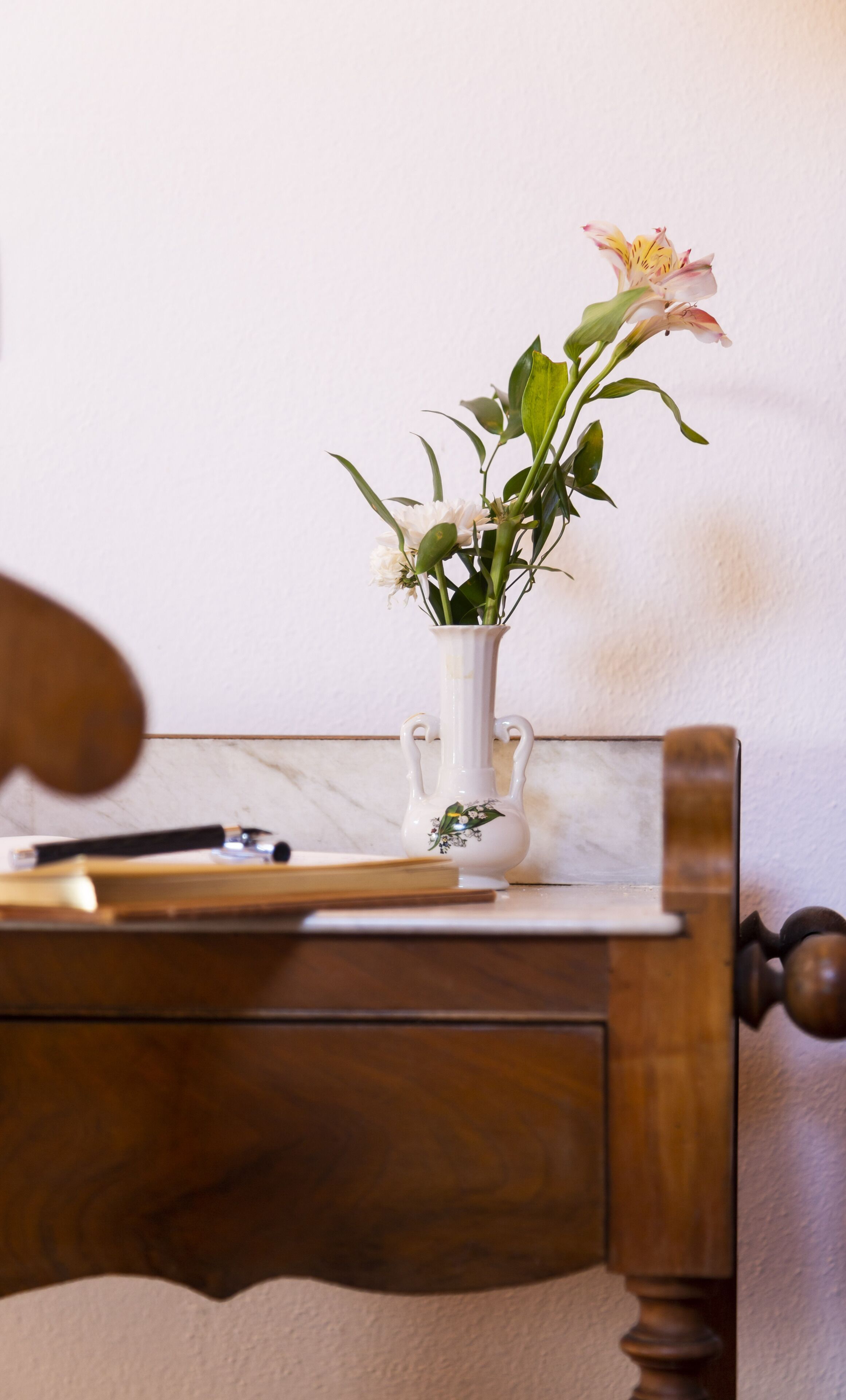Uma escrivaninha de madeira com um vaso branco contendo flores e uma caneta.