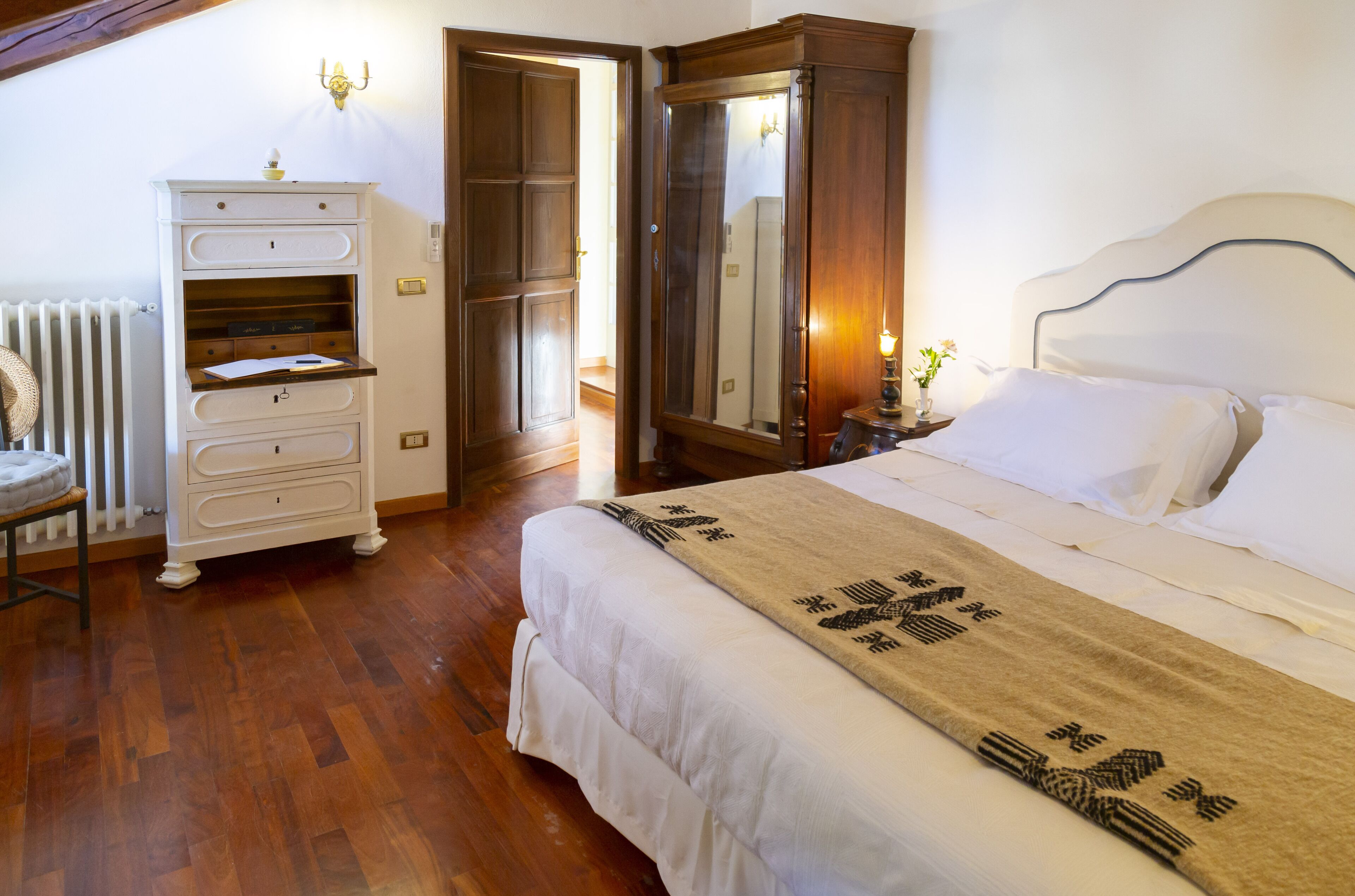 A bedroom with a large bed, a dresser, a wardrobe, and a radiator.