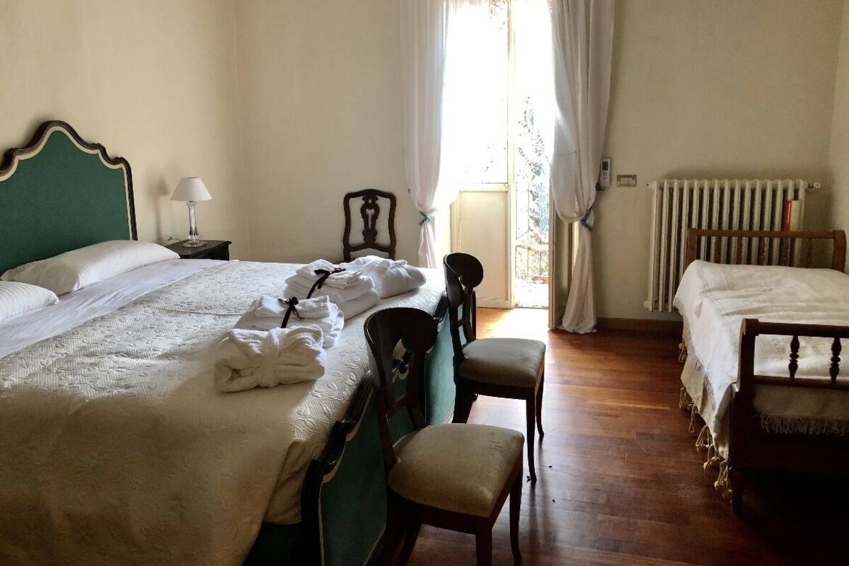 Ein Hotelzimmer mit einem großen Bett, einem Sessel, einem Nachttisch, einem Heizkörper und einem fenster mit Vorhängen.