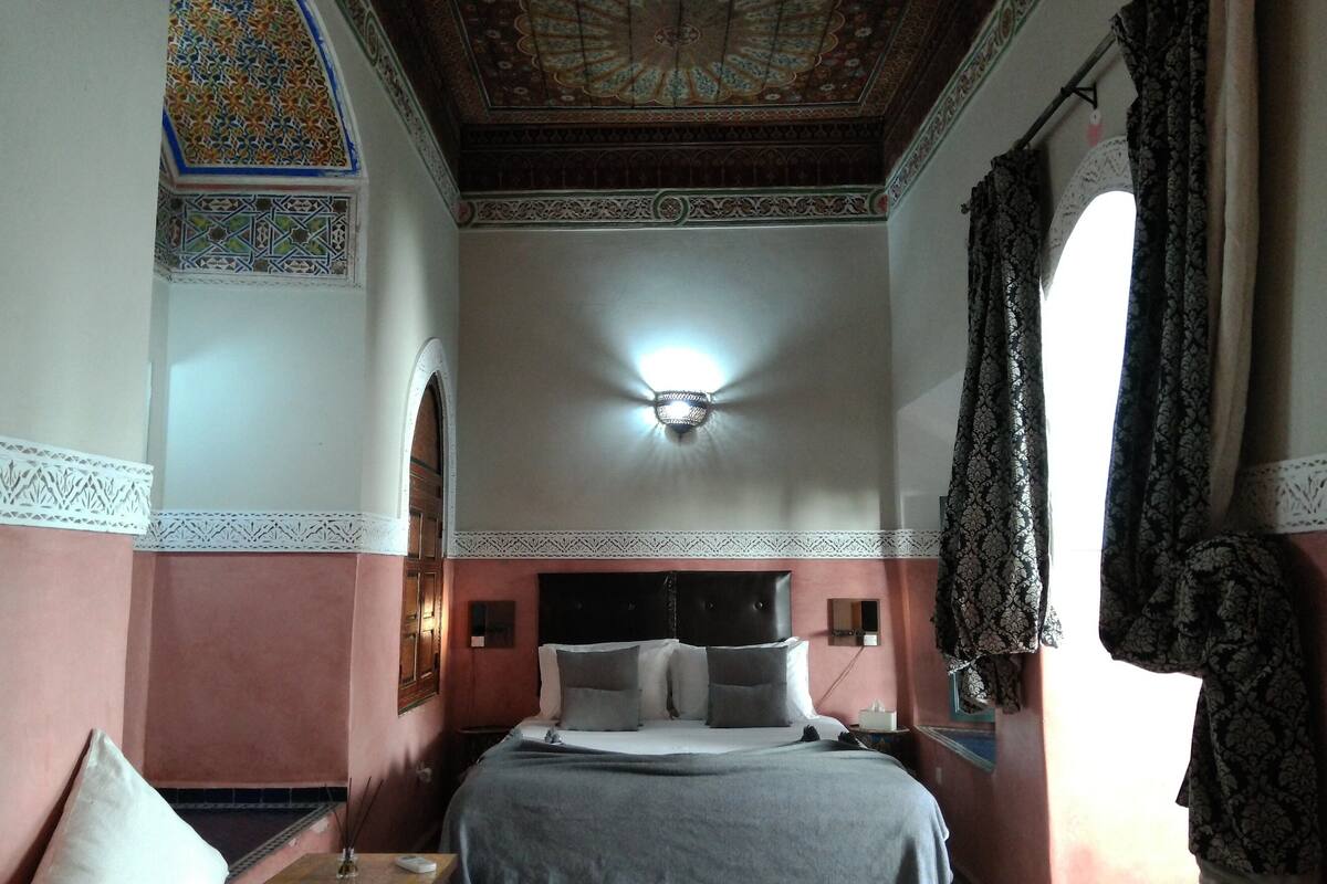 A bedroom with a bed, a nightstand, a wall-mounted lamp, and a decorative ceiling.
