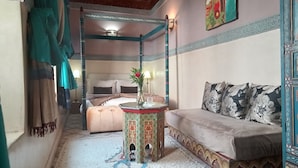 A room with a four-poster bed, a sofa, a small table with a vase, and a patterned rug. - Riad Maizie (Marrakech)