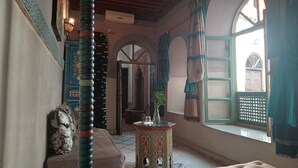A traditional room with a patterned wall, a wooden door, a small table with a vase, and a window with curtains. - Riad Maizie (Marrakech)