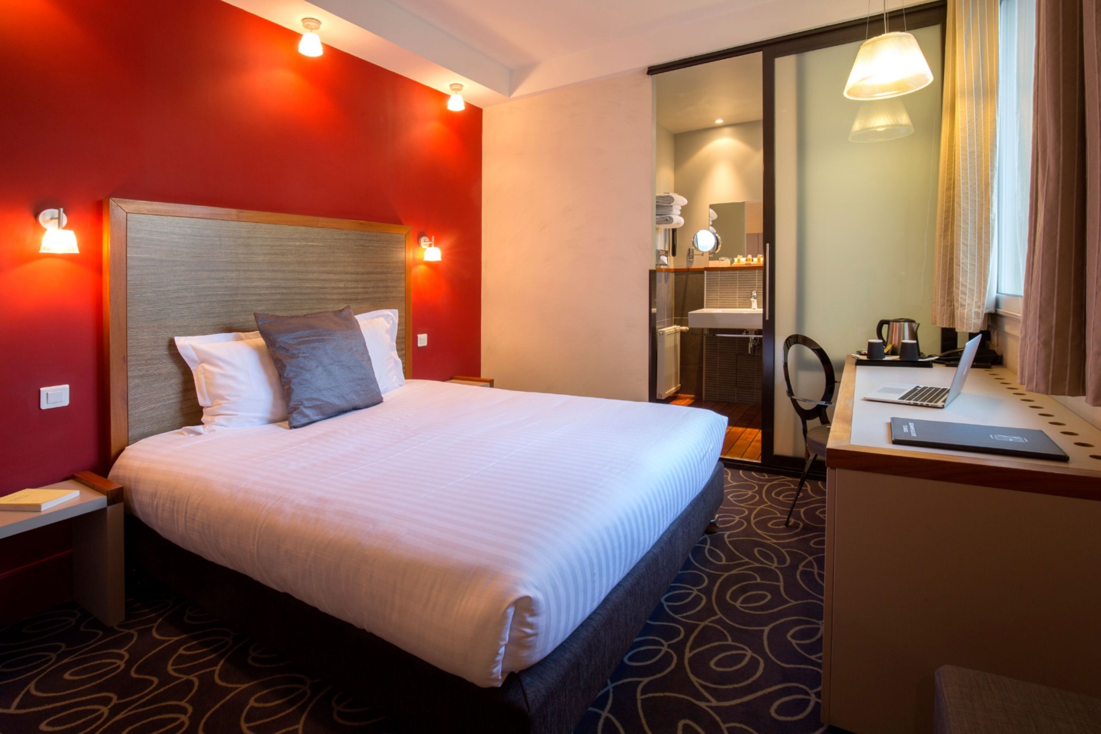 A hotel room with a large bed, a desk with a laptop, and a mirror.