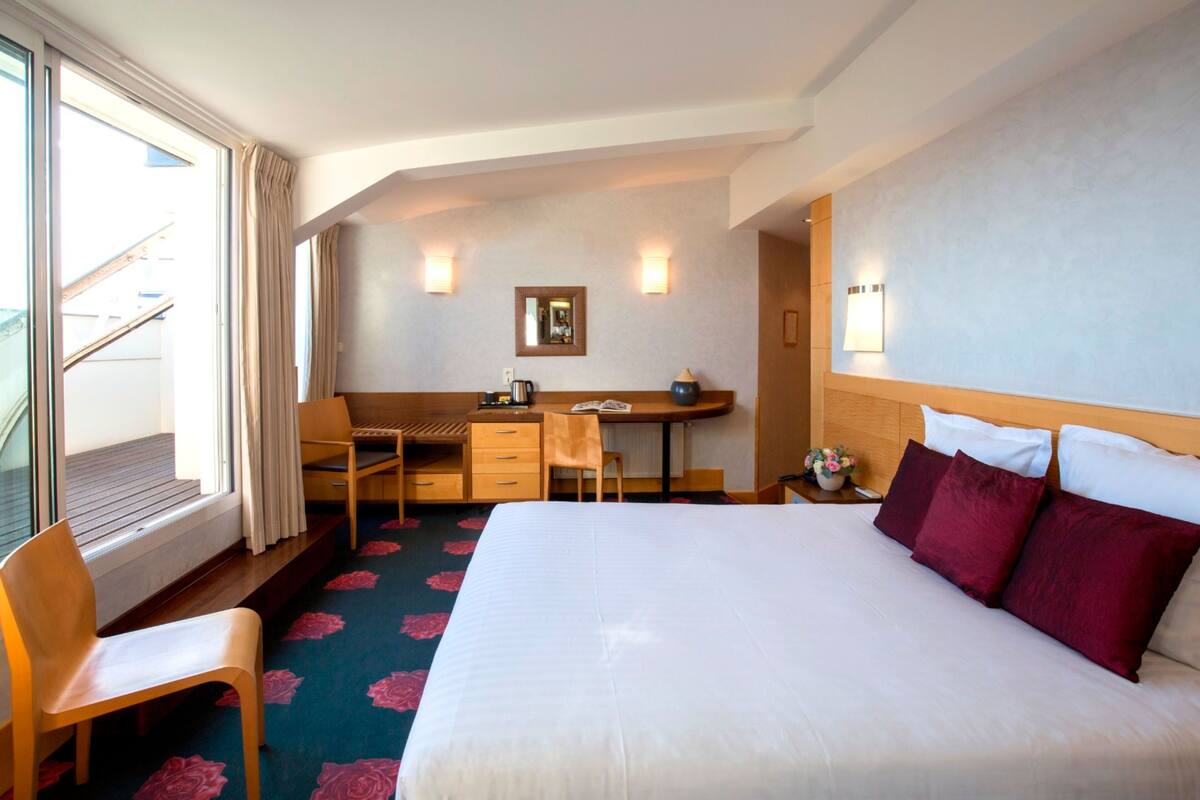 Habitación de hotel con una cama grande, un escritorio, una silla, una mesita y una ventana con cortinas.