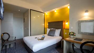 A hotel room with a bed, a desk, a chair, and a TV.