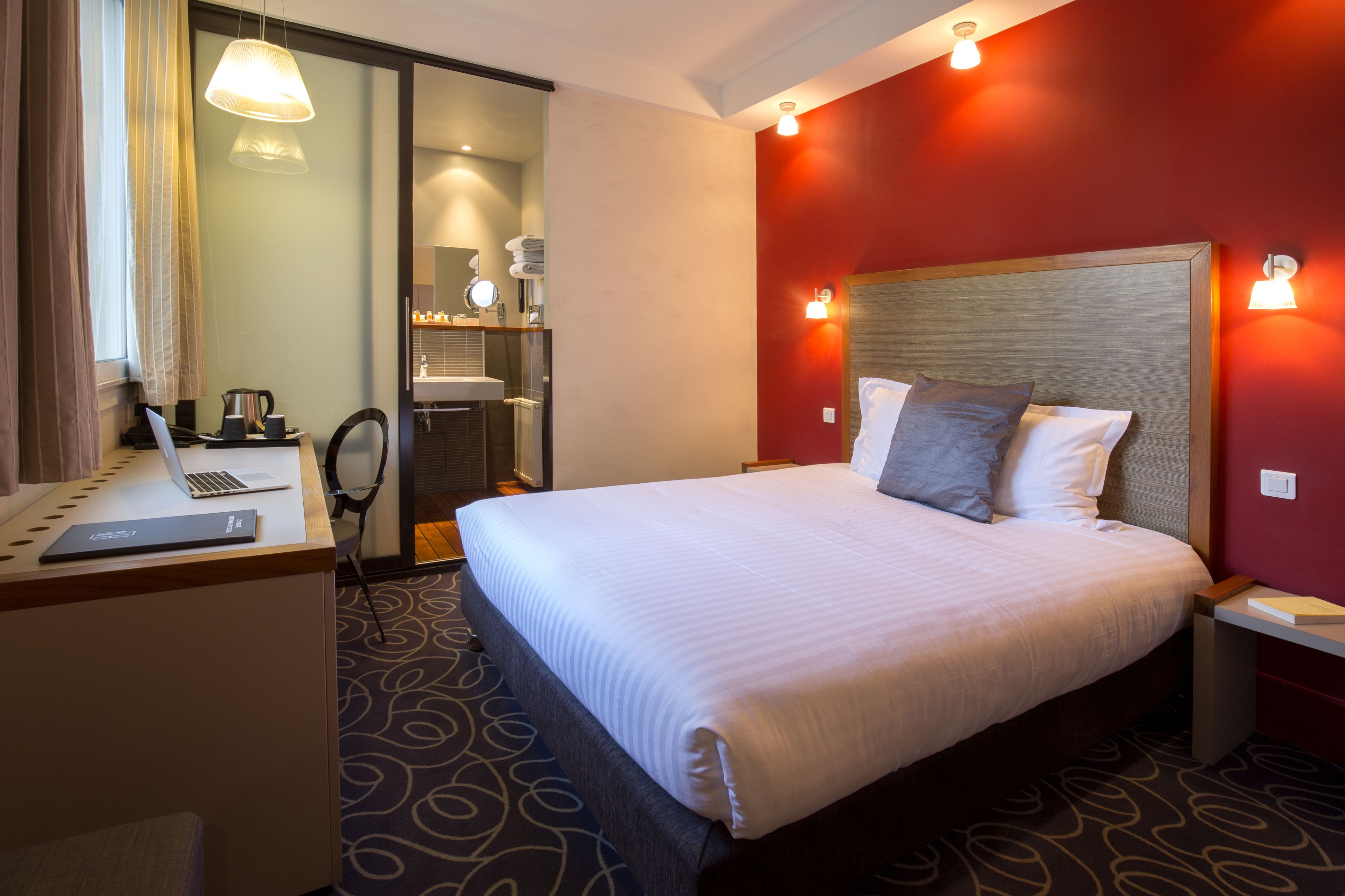 A hotel room with a large bed, a desk with a laptop, a mirror, and a shower area.