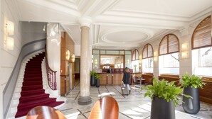 Un hall d’hôtel doté d’un magnifique escalier, d’un comptoir d’accueil et de plusieurs espaces où s’asseoir.
