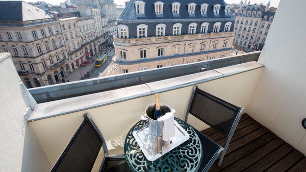 Un balcon avec une table et des chaises, une bouteille de champagne et une vue sur des bâtiments historiques.