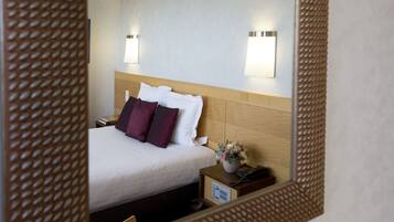 A hotel room with a bed, a nightstand, a lamp, and a mirror.