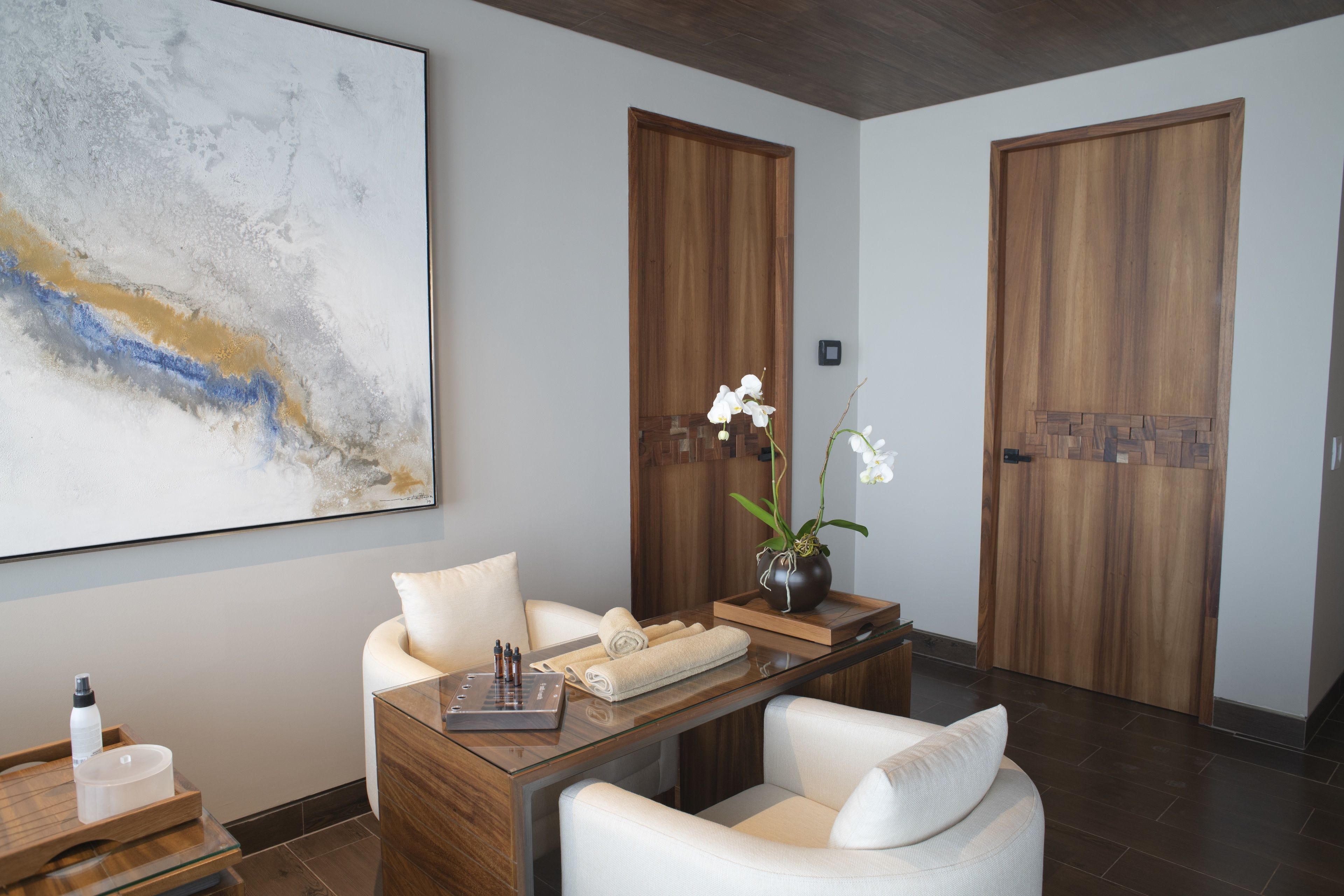 Eine moderne Hotelhalle mit einem Holzbüro, weißen Sesseln, einem großen abstrakten Gemälde und zwei Holztüren.