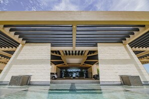 Un edificio moderno con una entrada amplia, una piscina y dos coches estacionados afuera.