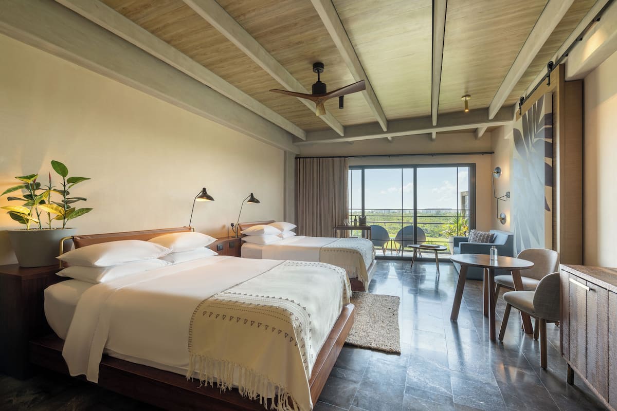 A hotel room with two beds, a dining area, and a balcony with a view.
